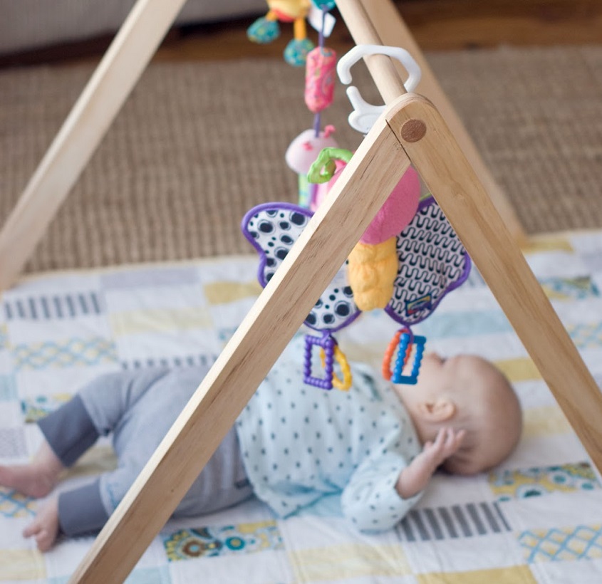 picture of a baby on the floor under a gym with toys 