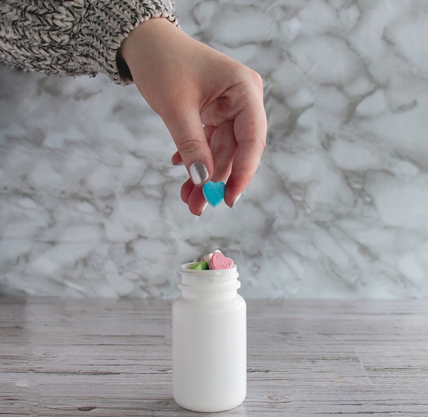 picture of a persons hand holding a pill in heart form, from a white bottle  on marble background 