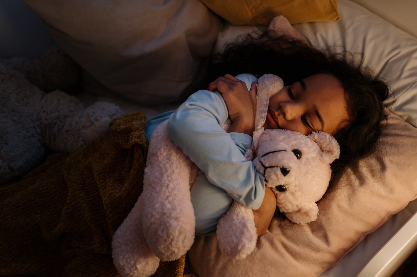 picture of a kid sleeping in bed hugging a teddy bear