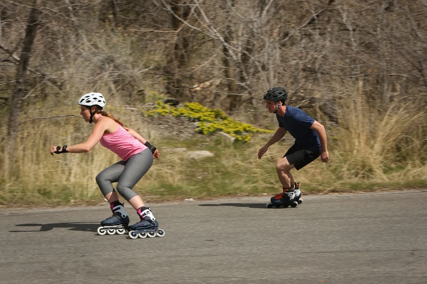 picture of two persons riding inline skates on a road beside a woods