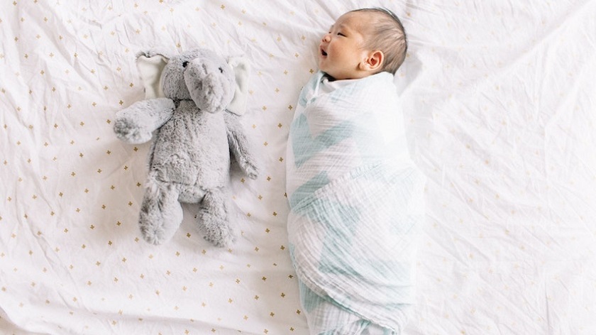 picture of a baby in a cosy wrap on a bed beside a plush toy