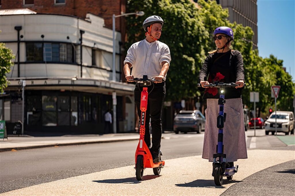 a man and a woman wearing safety helmets and riding scooters